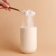 Spoon pouring Nutra Organics Organic Whey Protein - Vanilla 750g powder into a glass of milk on a beige background.