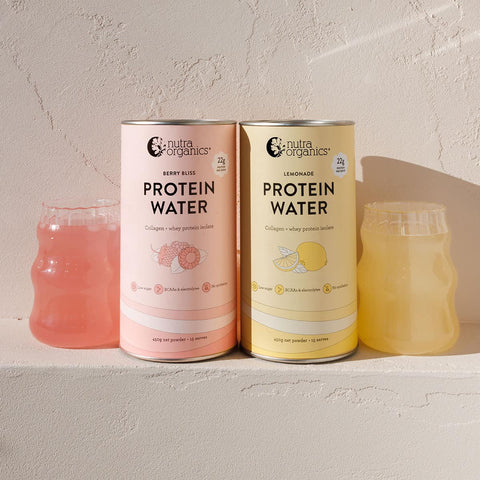 Two cans of Nutra Organics Protein Water on a light surface with glasses of berry and lemonade-flavored water.