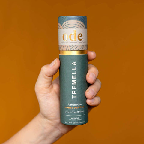 Hand holding tube of Tremella Mushroom Honey Pearls against an orange background. 