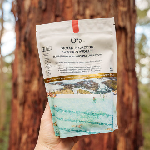 Hand holding 480g pouch Ora Organic Greens Superpowder+, vegan supplement to support energy, gut health, immunity, and detox.