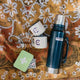 Blue Stanley thermos with two white mugs and green first aid tin on a floral picnic blanket.