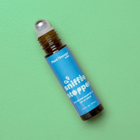 A roll-on bottle of Plant Therapy essential oil blend by sniffle stopper, featuring a bright blue label and amber glass bottle, set against a solid light green background.