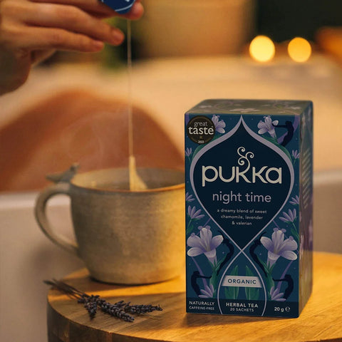 Pukka night time tea box with a steaming cup of tea and lavender on a wooden surface.
