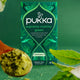 Pukka supreme matcha green tea packaging with green tea powder and leaves on a green background