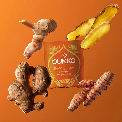 Pukka three ginger packaging with fresh ginger roots on an orange background