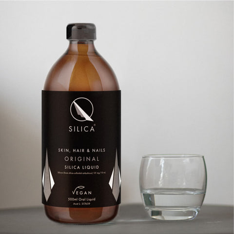 Amber bottle of Qsilica liquid with a black label next to an empty glass on a light grey background.
