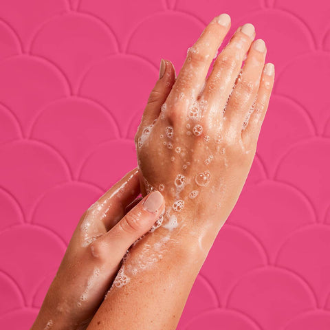 Hands with soap bubbles against a pink patterned background.