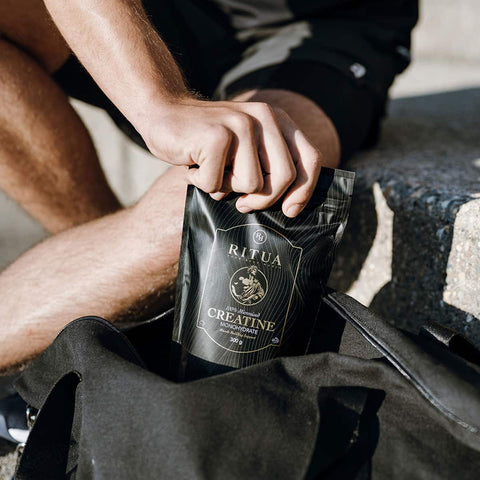 Person holding a black package labeled 'Ritua Creatine' on a stone surface.