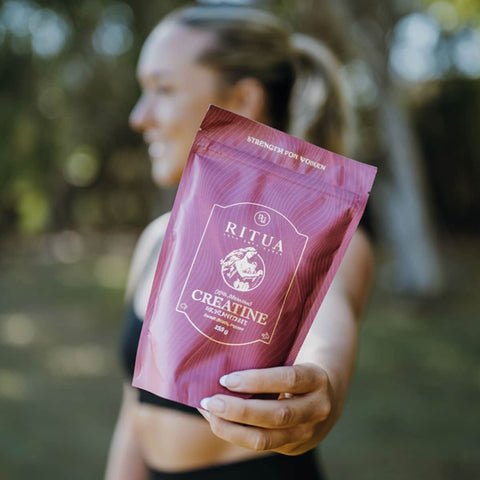 Person holding a purple package of Ritua Creatine in an outdoor setting.