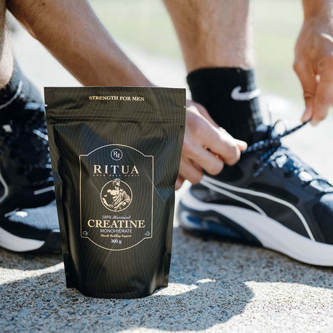 Hand tying shoelace next to black packaging of Ritua Creatine - Strength For Him 300g. 