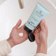 Person holding a tube of 'sanctum' cream with a small amount on their palm.