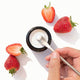 Hand scooping Solid Toothpaste Strawberry with Fluoride from a jar, surrounded by strawberries on a white background