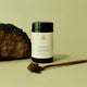 Jar of Chaga powder with a spoonful of powder and a piece of chaga mushroom on a green background