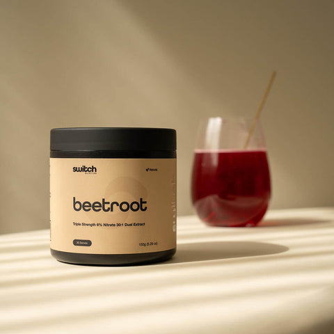 Container labeled 'switch beetroot' on a surface with a glass of red liquid in the background.