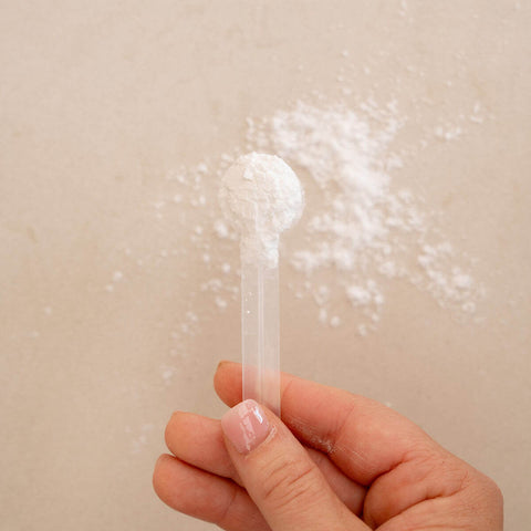 Hand holding a white powder sample against a beige background.
