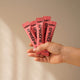 Hand holding pink packets of switch creatine against a beige background.