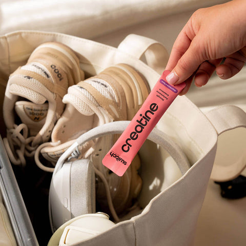 Person holding a pink creatine supplement stick in front of a bag with white sneakers.
