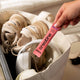 Person holding a pink creatine supplement stick in front of a bag with white sneakers.