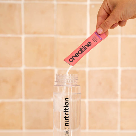 Person pouring creatine from pink sachet into a clear drink bottle.
