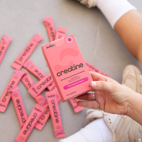 Person holding a pink 'switch' creatine supplement box with multiple packets on a gray surface.