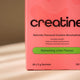 Pink box of creatine supplement with text on a beige background.