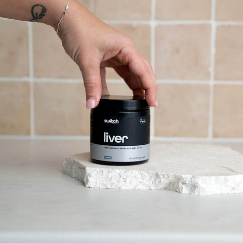 Person holding a jar labeled 'switch liver' on a white surface with a tiled wall background.