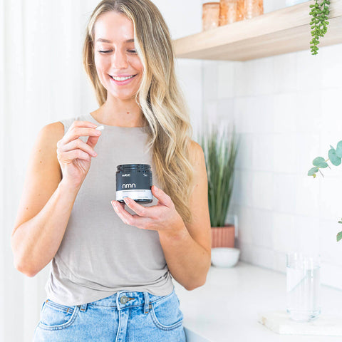 Woman holding a container of nmn in a kitchen setting.