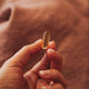 Hand holding a gold-colored capsule against a blurred brown background.