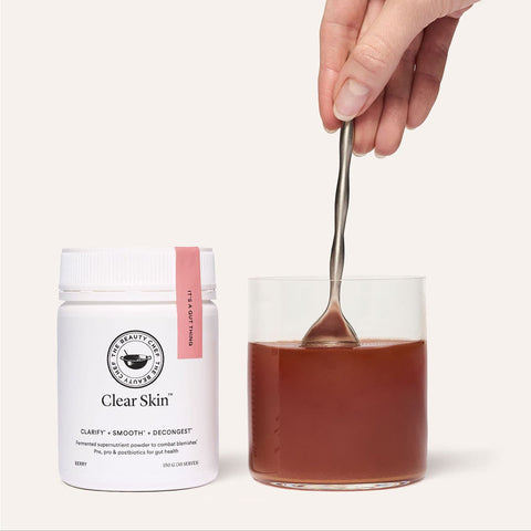 The Beauty Chef Clear Skin 150g product jar with a glass of red liquid & spoon on a white background.