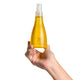 Hand holding a yellow bottle of jojoba oil with a white spray nozzle against a white background.