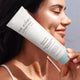 Woman holding a tube of 'The Jojoba Company' Citrus Gel Cleanser against a neutral background