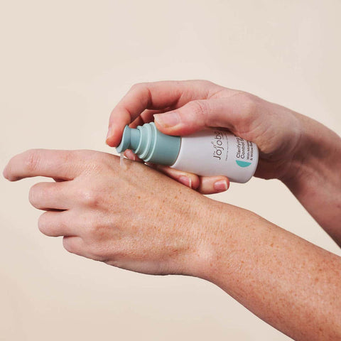 Hand applying a skincare product to another hand against a beige background