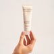 Hand holding a tube of 'The Jojoba Company' hydrating peptide day cream against a light background.