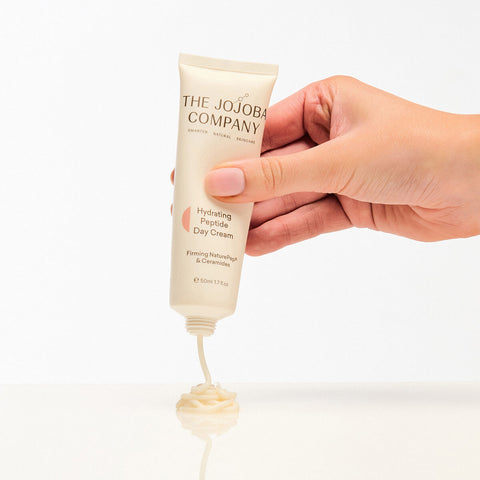 Hand holding a tube of 'The Jojoba Company' cream with visible cream at the base.