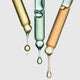 Three pipettes with droplets of different coloured serums on a light grey background