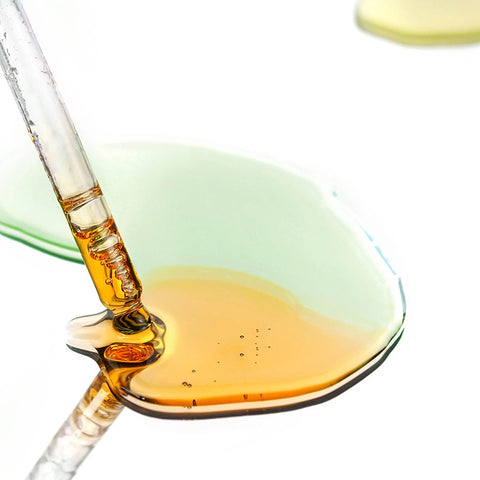 Amber liquid being dispensed from a dropper into a dish on a white background