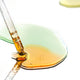 Amber liquid being dispensed from a dropper into a dish on a white background