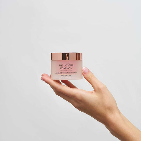 Hand holding a product from The Jojoba Company on a white background.