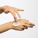 Hand applying cream to another hand on a white background