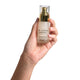 Hand holding serum bottle labeled 'The Jojoba Company Ultimate Serum' against a white background. Firming collagen.