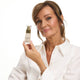 Mature woman holding bottle of The Jojoba Company Ultimate Serum near her face, showing her glowing complexion. 