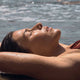 Model laying on the beach in the sun with droplets of water on her arm and sea in the background.