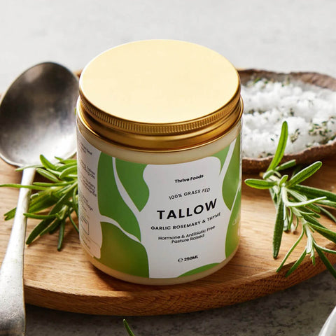 Jar of tallow with a gold lid on a wooden board with herbs and a spoon.