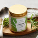Jar of tallow with a gold lid on a wooden board with herbs and a spoon.