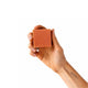 A hand holding a square, terracotta-colored soap bar against a solid white background.