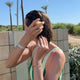 A woman outdoors with wet hair using a solid conditioner bar, standing in front of a tiled wall with palm trees and blue sky in the background.