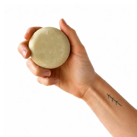 Hand holding a beige bar of soap against a white background.