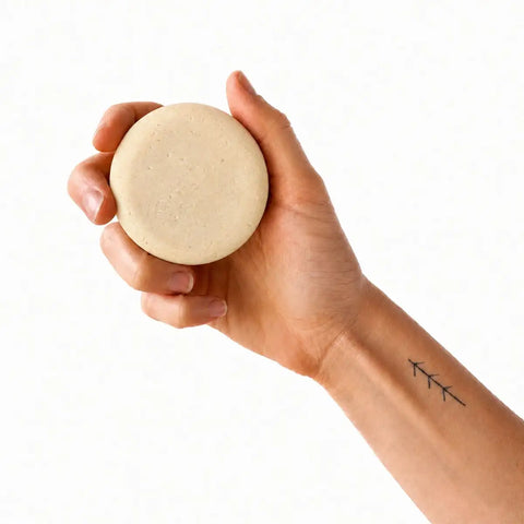 Hand holding a beige bar of soap against a white background.