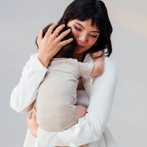 Woman holding a baby close to her chest against a plain background.