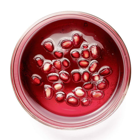 Pomegranate seeds in a clear glass bowl on a white background.
